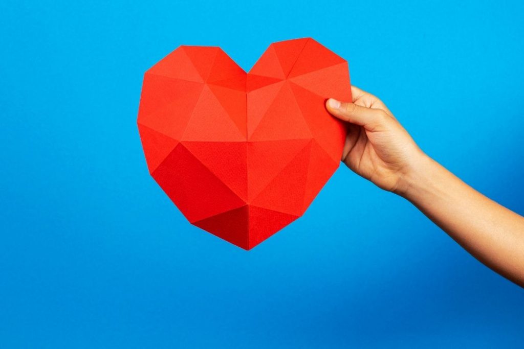 child's hand holding red paper heart
